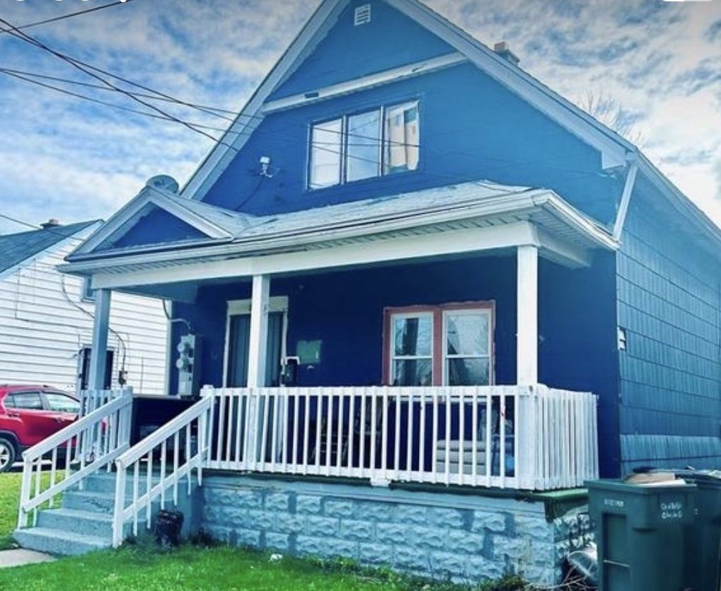 Blue house with a white railed porch and tidy front lawn in Buffalo, New York